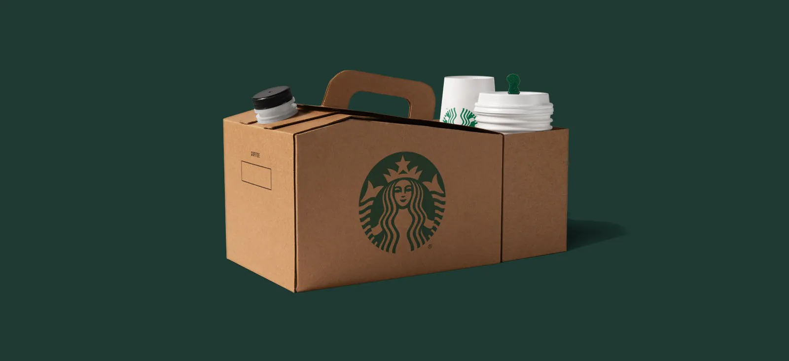 A Starbucks Coffee Traveler carrier, a brown cardboard box with a handle, a pour spout and the Starbucks siren logo, with white Starbucks cups and lids tucked in one end, on a dark green background