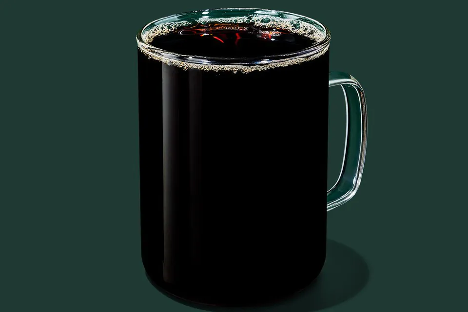 A clear glass mug of Starbucks Pike Place Roast brewed black coffee on a dark green background