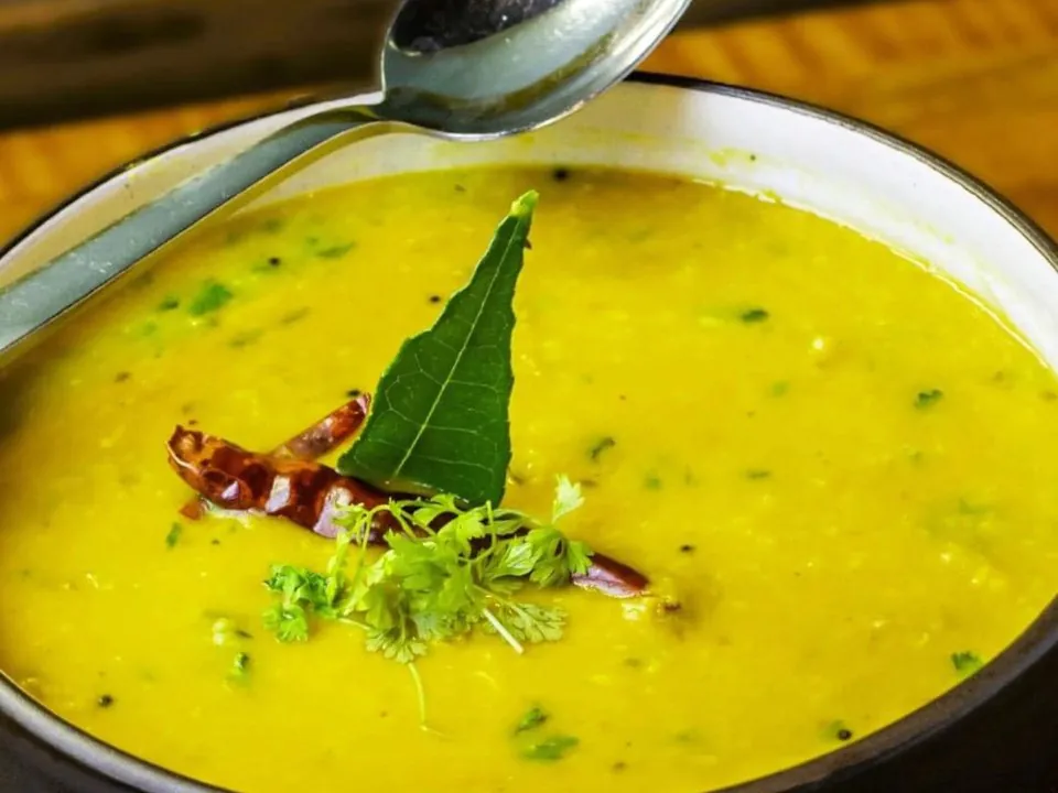 A bowl of yellow lentil dal with a curry leaf, a dried red chili and cilantro on top