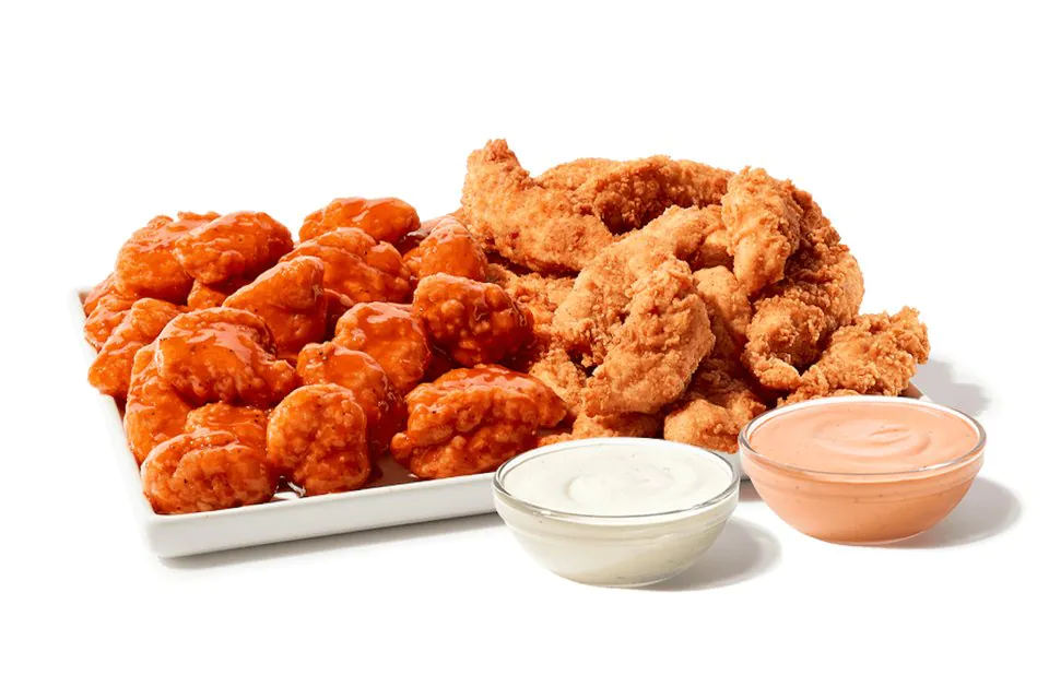 A Zaxby's Zampler Platter of sauced boneless wings and hand-breaded Chicken Fingerz on a white tray beside cups of Ranch and Zax Sauce